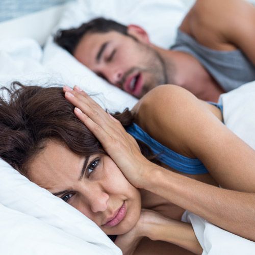 Man snoring next to annoyed woman